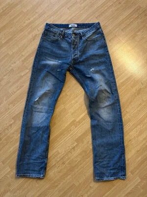 Blå raka jeans från Acne Studios - Snygga blå jeans från Acne Studios med raka ben och klassisk femficksmodell. Jeansen har slitna detaljer och en liten reva på ena benet för en cool, avslappnad look. Perfekta till vardagsstilen och lätta att matcha med det mesta.
