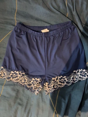 Blå shorts med spetskant - Snygga blå loungewear-shorts med elastisk midja och dekorativ vit spetskant längst ner. Perfekta för att chilla hemma eller sova i. Mjukt och bekvämt material som känns skönt mot huden.