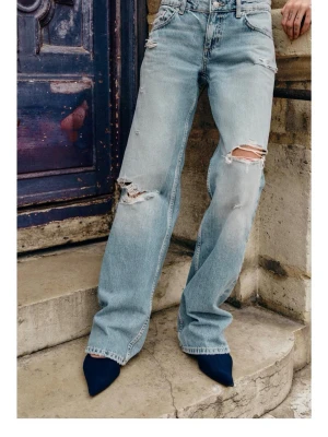 Ljusblåa raka slitna jeans - Säljer ett par ljusblåa jeans med raka ben och slitningar på både lår och knän. Jeansen har hög midja och klassisk femficksmodell. Perfekta för en avslappnad och trendig look. Materialet är denim i bomull.