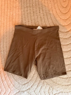 Bruna cykelshorts i bomull - Bruna cykelshorts i mjukt bomullstyg med elastisk midja och clean, minimalistisk design. Modellen har normal passform och slutar mitt på låret. Perfekta för sommaren och enkla att styla till olika looks.