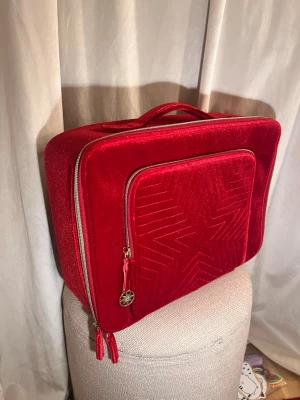 Röd sammetnessesät  - Snygg nessesär i röd sammet från Estee Lauder med ett elegant stjärnmönster på framsidan. Nessesären har ett stort fack och en framficka med guld dragkedja och dekorativt hänge. Praktiskt handtag upptill och mjuk, lyxig känsla. Den är värd ungefär 250kr💗