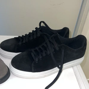 Svarta sneakers med vit sula - Stilrena svarta sneakers med ovandel i mockaliknande material och klassisk vit sula. Skorna har svarta skosnören och en låg profil som passar till många olika outfits. Perfekta för dig som gillar en clean och enkel look. Skorna har jag använt en gång 