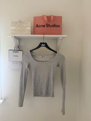 Ljusgrå långärmad topp med rund ringning - Supermjuk och stretchig ljusgrå topp med lång ärm och bred, rundad urringning. Sitter tight och är perfekt att styla med jeans eller kjol. Enkel och stilren design som passar till många olika looks.