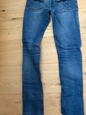 Nudie jeans - Ett par blå skinny jeans med slitningar och tvättade detaljer. Jeansen har klassisk femficksdesign och smal passform hela vägen ner. Perfekta för en avslappnad och trendig look.