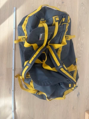 the north face duffel bag - Säljer en stor duffelbag i slitstark grå nylon med gula detaljer och remmar. Väskan har flera bärhandtag och justerbara axelremmar så den kan bäras som ryggsäck. Perfekt för resor eller träning när du behöver mycket packutrymme.