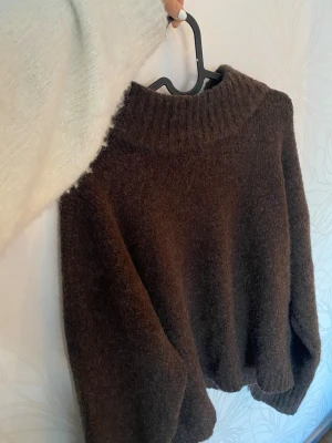 Brun stickad tröja med liten polokrage - Mysig brun stickad tröja från Nelly med  liten polokrage. Tröjan har långa ärmar och ribbade muddar vid ärmslut och nederkant. Använd fåtal gånger och är i mycket bra skick.