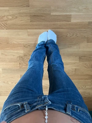 Mörkblå bootcut jeans med låg midja - Säljer ett par mörkblå bootcut jeans med låg midja och klassiska fem fickor. Jeansen har kontrastsömmar och bälteshällor, perfekta för en avslappnad och trendig look. Materialet är denim i bomull med lite stretch för extra komfort.