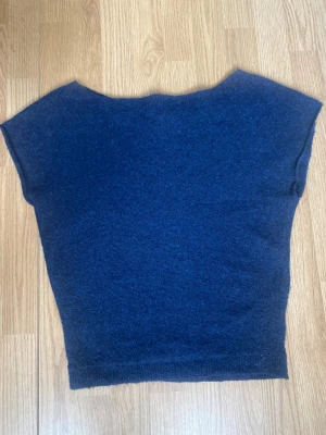Mörkblå Nelly stickad topp med kort ärm - Mysig mörkblå stickad topp med korta ärmar och bred halsringning. Enkel och stilren design som passar perfekt till jeans eller kjol. Mjuk och skön kvalitet, troligtvis i ull- eller akrylblandning. Knappast använd 