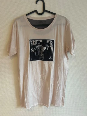 Beige t-shirt med fototryck Limitato - Säljer en beige t-shirt från Limitato med ett svartvitt fototryck på bröstet. T-shirten har rund hals och korta ärmar. Perfekt för dig som gillar stilrena plagg med en twist.
