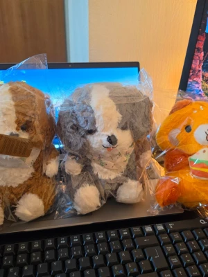 Tre mjukisdjur hund och björn - Säljer tre söta mjukisdjur: två hundar i brunt och grått med vita detaljer samt en orange björn som håller en hamburgare. Alla är tillverkade i mjukt plyschmaterial och har rund form. Perfekta som dekoration eller present.