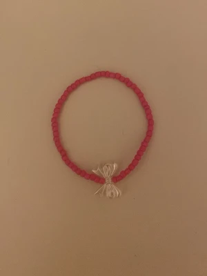 Rosa pärlarmband med rosett - Sött armband med små rosa pärlor och en dekorativ rosett i silverfärgad metall. Armbandet har en enkel och ungdomlig stil som passar perfekt till din vardagslook. Elastiskt band gör det lätt att ta på och av.
