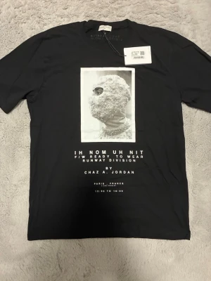 Svart t-shirt IH NOM UH NIT - Säljer en svart t-shirt från IH NOM UH NIT med ett stort grafiskt tryck framtill och textdetaljer. T-shirten har rund hals och korta ärmar. Materialet känns mjukt och skönt, perfekt för en trendig streetwear-look. Passar M står XL