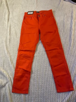 Orange jeans från Filippa K - Snygga orange jeans från Filippa K med klassisk femficksmodell och raka ben. Jeansen har silverfärgade nitar och knapp, samt bälteshällor. Perfekta för dig som vill sticka ut med färg i din outfit.
