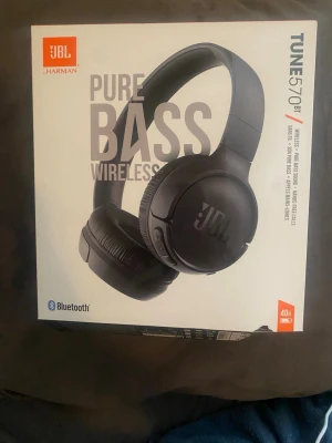 JBL Tune 570BT  - Säljer ett par svarta JBL Tune 570BT trådlösa on-ear hörlurar med Pure Bass-ljud och Bluetooth. Hörlurarna är hopfällbara och kommer med en orange USB-laddningskabel. Perfekta för musik och samtal med upp till 40 timmars batteritid. Har aldrig använts!!