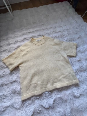 Ljus gul  stickad t-shirt från Gina Tricot - Kortärmad stickad t-shirt i ljus gul från Gina Tricot. Tröjan har rund halsringning med ribbstickade detaljer vid hals, ärmslut och nederkant. 