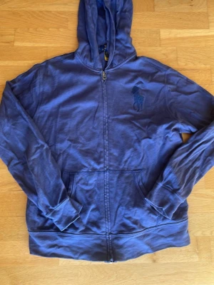 Blå zip hoodie från Polo Ralph Lauren - Snygg blå hoodie med dragkedja från Polo Ralph Lauren. Klassisk huva, två fickor framtill och den ikoniska broderade loggan på bröstet. Tillverkad i mjukt bomullsmaterial som är skönt att bära. Perfekt för en avslappnad och stilren look. storlek 14-16 år. Jag sk flytta så måste bli av med grejer därav priset