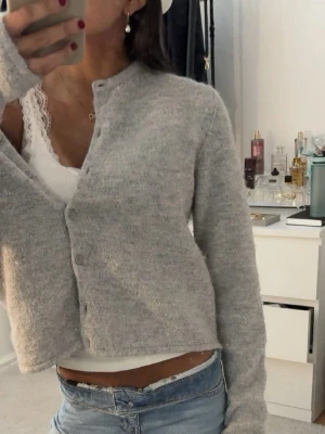 Ljusgrå mjuk kofta - Superfin ljusgrå kofta med rund halsringning och knappar framtill. Koftan är i ett fluffigt, mjukt material och har en något kortare passform💞