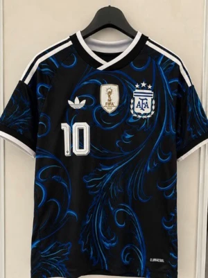 Argentina Messi matchtröja svart/blå - Snygg Argentina matchtröja i svart med blått mönster, nummer 10 och Messi på ryggen. Tröjan har vita detaljer, AFA-logga, FIFA-märke och klassiska ränder på axlarna. Perfekt för dig som älskar fotboll och vill sticka ut på planen.