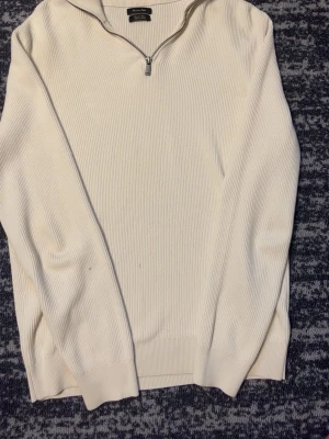 Vit ribbstickad massimo dutti tröja med halvzip - Snygg vit ribbstickad tröja med halvzip och hög krage. Tröjan har långa ärmar och ribbade muddar vid ärmslut och nederkant. Perfekt för lager på lager och enkel att matcha med olika outfits.