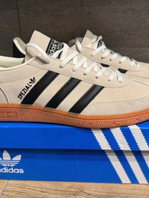 Adidas Spezial beige sneakers - Snygga Adidas Spezial sneakers i beige mocka med klassiska svarta ränder på sidorna och gummisula. Skorna har vita snören och låg profil, perfekt för en clean och stilren look. 