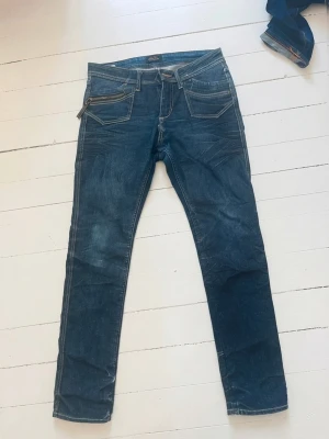 Blå jeans från SQIN, W29 - Snygga blå jeans från SQIN med raka ben och coola detaljer som dragkedja på fickan. Klassisk femficksmodell i slitstarkt denimtyg med kontrastsömmar. Perfekta för en avslappnad och trendig look.
