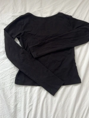 Svart långärmad topp - En enkel svart långärmad topp med öppen rygg. Tillverkad i mjukt bomullsmaterial som känns skönt mot huden. Perfekt basplagg att styla till olika outfits. Tröjan är ifrån Gina Tricot i storleken 146-152. 
