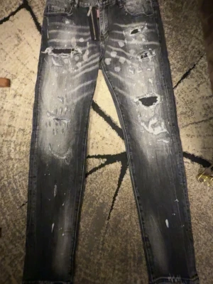 Dsquared2 slitna svarta jeans - Säljer ett par svarta jeans från Dsquared2 med slitningar, hål och blekta detaljer. Jeansen har klassisk femficksmodell, dragkedja och smal passform. Rå och trendig look som sticker ut.