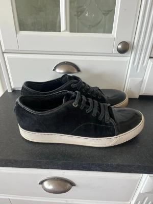 Lanvins - Snygga svarta sneakers med ovandel i mocka och tåparti i blankt lackmaterial. Skorna har svarta skosnören och en vit, tjock sula som ger en modern look. Perfekta för dig som gillar stilrena och trendiga skor.