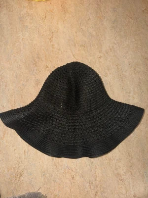 Svart solhatt med bred brätte - Snygg svart solhatt med bredt brätte och virkad struktur. Hatten har en mjuk och flexibel form som ger en avslappnad vibe. Perfekt accessoar för soliga dagar och passar till många olika outfits. Materialet känns lätt och luftigt.