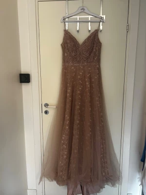 Beige långklänning med spetsdetaljer - Elegant beige långklänning med tunna axelband och v-ringad urringning. Klänningen har vackra spetsdetaljer och ett lager av tunn tyll som ger en romantisk känsla. Perfekt inför bal eller bröllop. Använt i ett fåtal timmar. Det finns ett hål i klänningen,  dm för mer bilder eller info❗️storlek 16, dvs 44