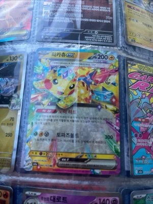 Pikachu EX Topaz Pokémonkort - Säljer ett färgglatt och glittrande Pikachu EX Pokémonkort med topaz-tema. Kortet har 200 HP och är på koreanska. Motivet visar Pikachu i en kristall-liknande design med regnbågsfärger och holografisk effekt. Perfekt för samlare av Pokémonkort.