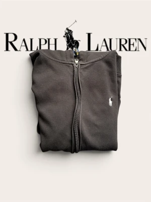 Svart hoodie från Ralph Lauren - Säljer en svart hoodie från Ralph Lauren med dragkedja framtill och klassisk vit logga på bröstet. Hoodien har huva, ribbade muddar och fickor framtill. Perfekt för en chill och stilren look. Materialet känns mjukt och bekvämt( Kommer med svart snöre)