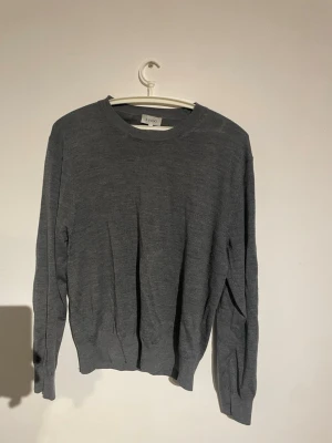Mörkgrå stickad tröja - En stilren mörkgrå stickad tröja med rund halsringning och långa ärmar. Tröjan har en enkel och klassisk design, perfekt för lager på lager under kyliga dagar. Tillverkad i mjukt material som känns skönt mot huden. Nypris 850kr