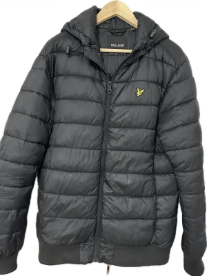 Svart vinterjacka från Lyle & Scott - Snygg svart vinterjacka från Lyle & Scott med huva och dragkedja framtill.                                  Storleken passar även de som tar på L storlek 