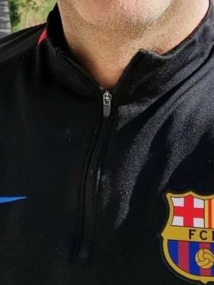 Svart FC Barcelona träningströja - Svart träningströja med FC Barcelona-emblem på bröstet och blå Nike-logga. Tröjan har röda detaljer längs ärmarna och en half zip-dragkedja vid halsen. Perfekt för fotbollsträning eller som sportig vardagströja.