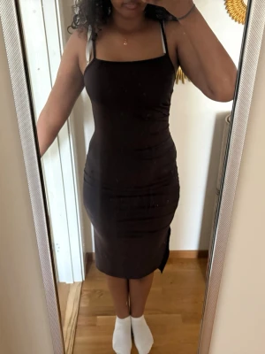 Svart tight midiklänning - Säljer en svart, tight klänning med smala axelband och rak urringning. Klänningen har en slits på sidan och är figurnära med en enkel, stilren design. Perfekt för dig som gillar minimalistisk stil.
