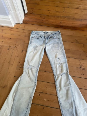 Lågmidjade ljusblå jeans med slitningar  - Säljer dessa jeans från abercombie & fitch som är omsydda till bootcut. Jeansen är lågmidjade och har slitningar på benen. Har tyvärr ingen bild med de på då de är försmå för mih. Midjemått 36 cm och innerbenslängd 75 cm. 