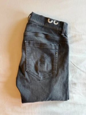 Dondup george jeans - Snygga mörkgrå slim fit jeans med klassisk femficksdesign och raka ben. Jeansen har en diskret logga på bakfickan och är tillverkade i mjukt denimtyg med lite stretch för extra komfort. Perfekta för en avslappnad och trendig look.