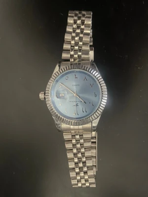 Silverfärgad klocka med blå urtavla rostfri äkta silver - Stilren klocka i silverfärgat metallarmband och ljusblå urtavla. Urtavlan har arabiska siffror och datumvisning. Klassisk design med räfflad kant runt boetten och länkarmband som ger en tidlös look.