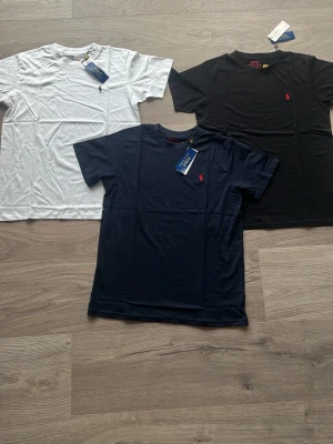 3-pack Polo Ralph Lauren t-shirts - Säljer ett 3-pack klassiska t-shirts från Polo Ralph Lauren i färgerna vit, svart och marinblå. Alla har korta ärmar, rund hals och den ikoniska broderade loggan på bröstet. Perfekta basplagg i mjuk bomull för en clean och stilren look. OBS tar inget under 499 då jag anser de dunder pris. 