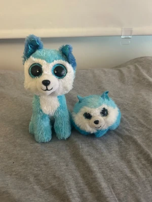 Två blåa gosedjur från Ty - Säljer två söta gosedjur från Ty, båda i blått och vitt plyschmaterial. Ena är en sittande hund med stora glittriga ögon och blå öron, den andra är en rundare variant med små öron och svans. Perfekta som dekoration eller samlarobjekt!