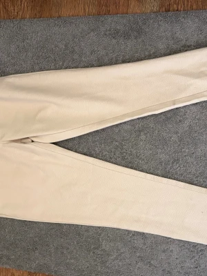 Beige mjukisbyxor från Lacoste - Säljer ett par snygga mjukisbyxor från Lacoste. Byxorna har en relaxed fit med resår i midjan och ett diskret Lacoste-märke i grönt vid fickan. Tillverkade i mjukt och bekvämt material som passar perfekt för chill dagar.