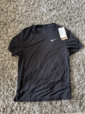 Svart Nike t-shirt med logga - En svart t-shirt från Nike med den klassiska vita swoosh-loggan på bröstet. T-shirten har rund hals och korta ärmar, tillverkad i ett mjukt och lätt material som passar perfekt till träning eller chill.