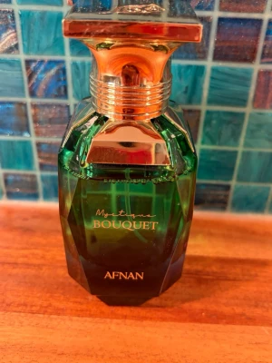 Afnan Mystique Bouquet parfym 80ml - Mystique Bouquet från Afnan är en Eau de Parfum i en elegant grön glasflaska med guldfärgat lock och detaljer. Flaskan rymmer 80 ml och har en lyxig, modern design som sticker ut på parfymhyllan. Använd ett fåtal gånger, som ny. 
