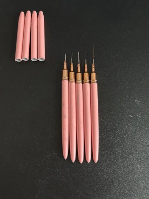 Rosa nail art penslar för nagellack - Säljer ett set med fem nail art penslar med smala, fina spetsar och rosa handtag. Perfekta för detaljerad nageldesign och kreativa mönster. Penslarna har guldiga detaljer och medföljer skyddande hylsor. Passar dig som vill skapa unika nagellooks hemma.