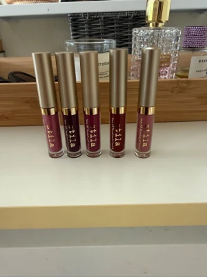 Stila flytande läppstift 5-pack - Säljer ett 5-pack flytande läppstift från Stila i olika nyanser av rosa, nude och vinrött. Läppstiften har guldfärgade lock och genomskinliga hylsor som visar färgen. Perfekt för dig som vill ha flera val till läpparna och gillar matta, pigmentrika färger.