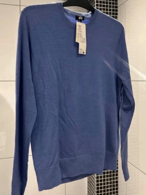 Blå merinoulltröja från Uniqlo - Storlek S. Taggen är ej kvar längre. Helt ny. Säljer en stilren blå stickad tröja från Uniqlo i extra fin merinoull. Tröjan har rund halsringning, långa ärmar och ribbade muddar. Perfekt för dig som gillar minimalistisk och bekväm stil. Maskintvättbar och supermjuk!
