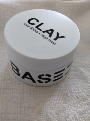 Vit hårlera BASES Low Shine High Hold - Säljer en oanvänd burk hårlera från BASES med texten 'Low Shine • High Hold'. Produkten innehåller bland annat sheasmör och arrowroot powder. Perfekt för dig som vill ha en matt finish och stark stadga till håret.