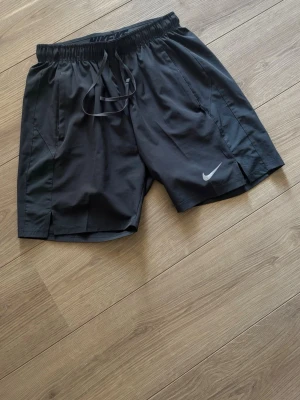 Gråa träningsshorts från Nike - Snygga svarta träningsshorts från Nike med elastisk midja och snörning. Shortsen har sidofickor och en liten slits på benen för extra rörelsefrihet. Perfekta för gymmet eller löprundan.