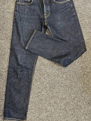 Nudie Jeans Solid Ollie Dry Abyss - Säljer ett par raw jeans från nudie med en taperd/straight passform. Köpte i julas och använda fåtal gånger pga det krympte mycket efter första tvätt och växte ur. Så i princip helt nya.  Hör av er ifall ni har några frågor eller prisförslag så kan vi förmodligen komma fram till något vid snabb affär.
